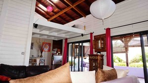 Een ruime woonkamer met een hoge plafond, houten balken en een schuifdeur naar een balkon.