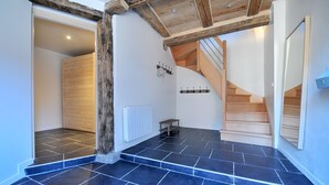A hallway with dark tiled flooring, wooden beams, a staircase, and a coat rack.