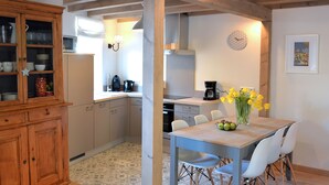 A compact kitchen with a dining area, featuring a wooden cabinet, a microwave, a coffee maker, and a vase with flowers on the table.