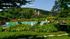 Ein Swimmingpool, umgeben von üppigem Grün, mit einer Kirche im Hintergrund.