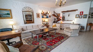 Een ruime woonkamer met een bank, fauteuil en salontafel, een trap en een keukenhoek.