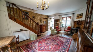 Een ruime woonkamer met een grote houten trap, een rood tapijt met dessin en een open haard.