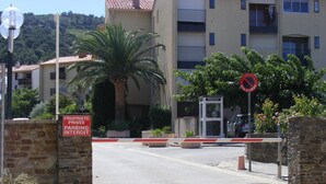 Un ingresso privato per parcheggi con un muro in pietra, un cartello che indica parcheggio riservato, una palma e un edificio sullo sfondo con balconi.