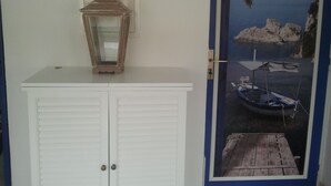 Un armadio bianco con anta in vetro e uno specchio sopra, una porta con cornice blu e un poster con una barca ormeggiata.