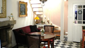A living room with a fireplace, a dining table with chairs, a staircase, and a door with a wreath.