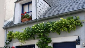 A white building with blue doors and windows, covered in greenery and red flowers.
