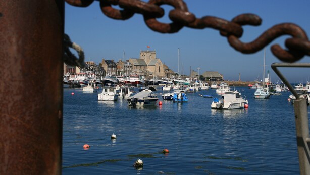 A harbor with multiple boats docked, a prominent building with a tower, and a rusty chain in the foreground.