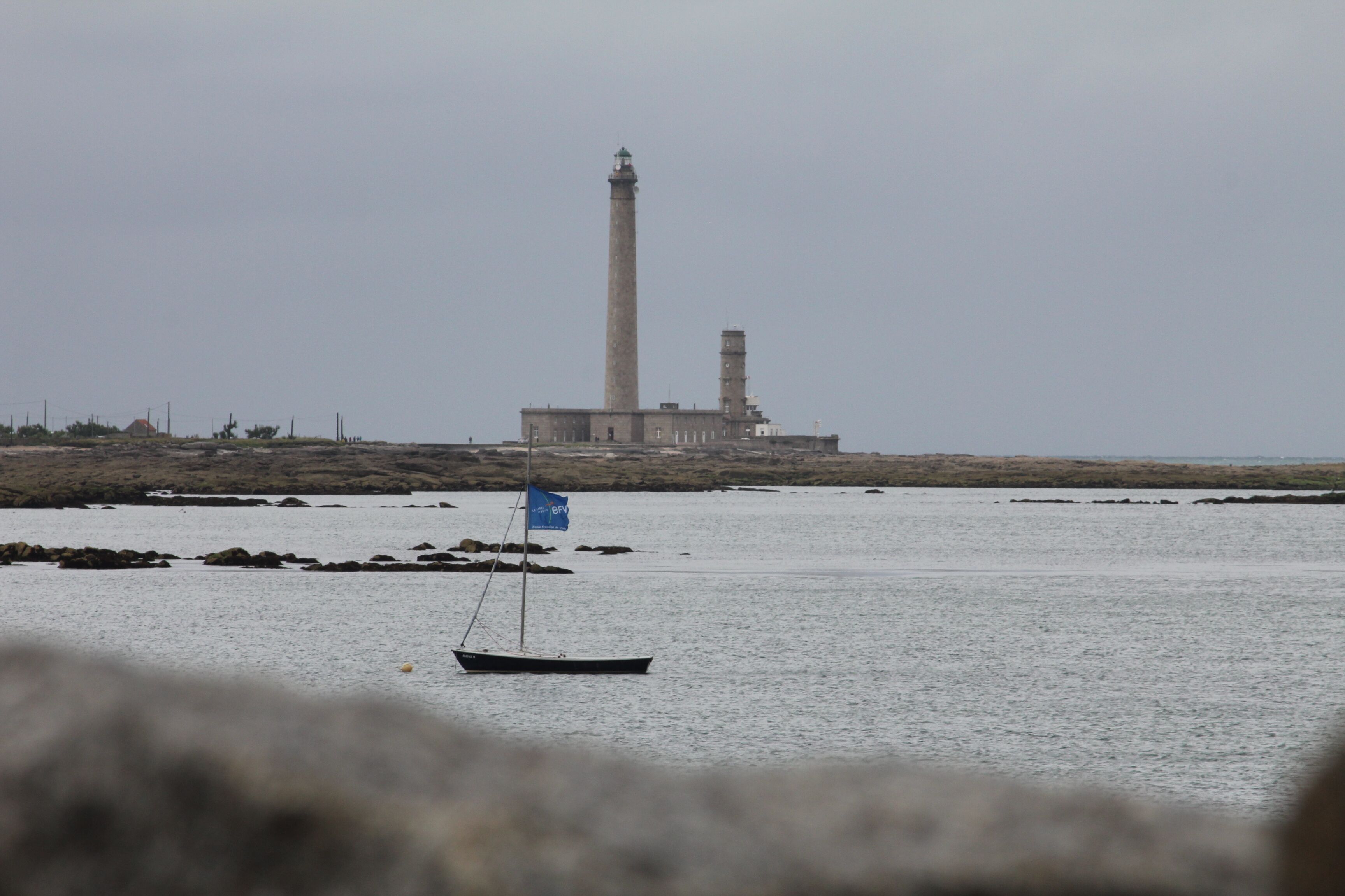 Un faro su una costa rocciosa, con una piccola imbarcazione in primo piano.