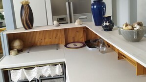 Een moderne keuken met een inbouwoven, een magnetron en een roestvrijstalen koelkast. Er staan rieten manden op planken en een houten snijplank op het aanrecht.