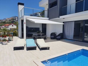 Un espace piscine extérieur moderne, doté de chaises longues et d’un coin salon abrité.