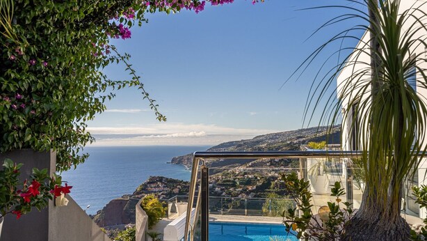 Vista de la piscina con una clara vista al océano, una pileta y vegetación circundante.
