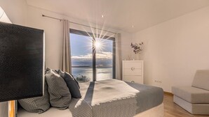 Un dormitorio con una cama grande, un televisor, un aparador y vistas al mar.