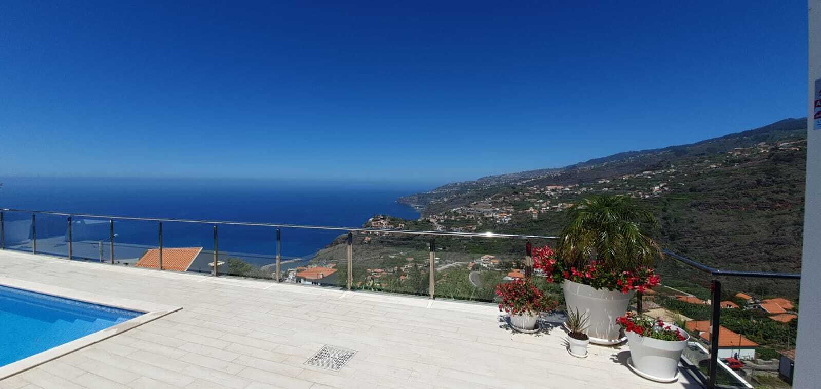 A rooftop pool with a clear view of the ocean and a hillside town.
