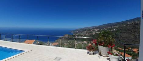 A rooftop pool with a clear view of the ocean and a hillside town.