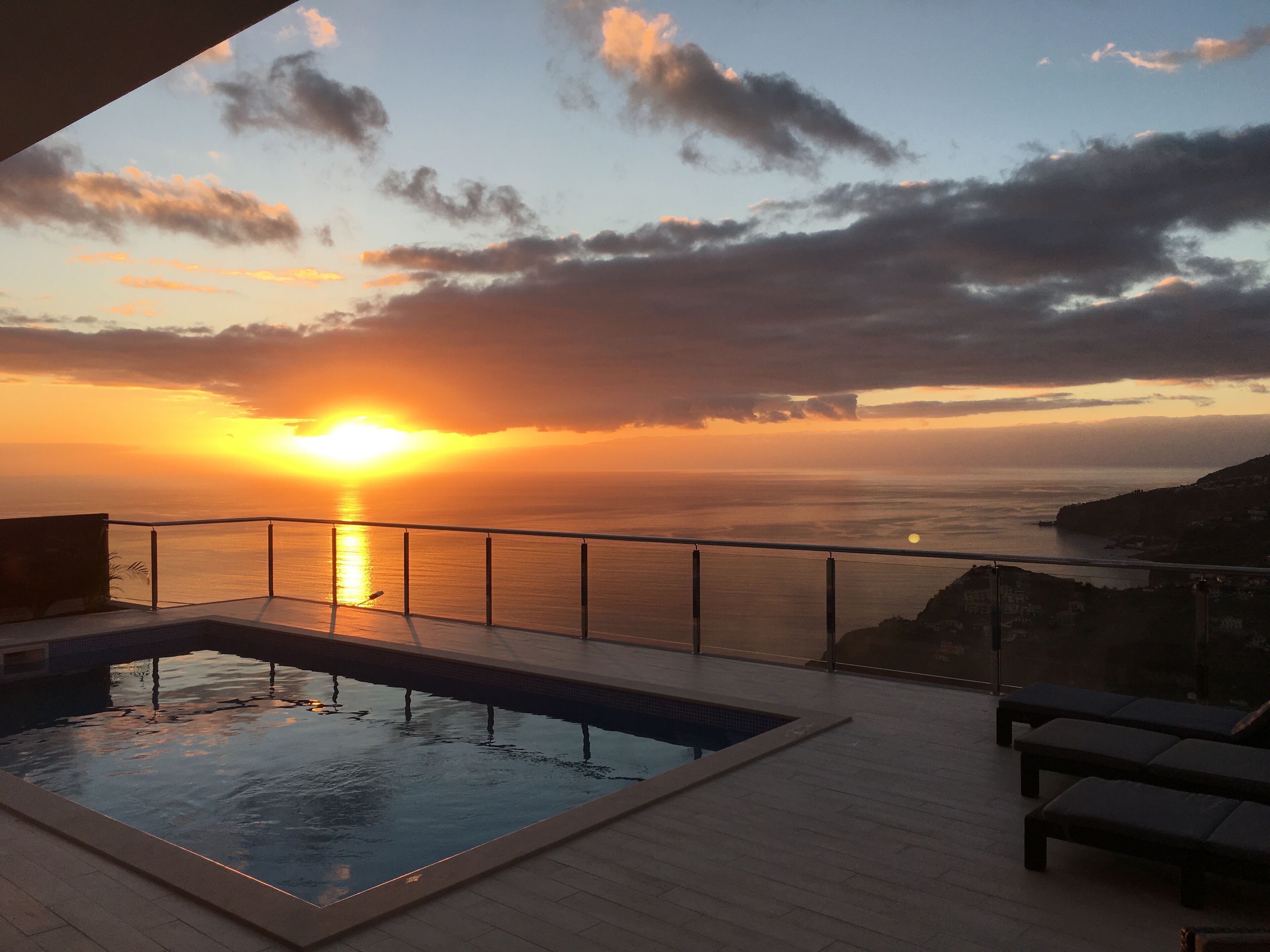 A pool with a sunset view, a railing, and lounge chairs.
