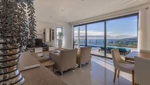 Un salón moderno con un ventanal grande con vistas a una piscina y al océano.