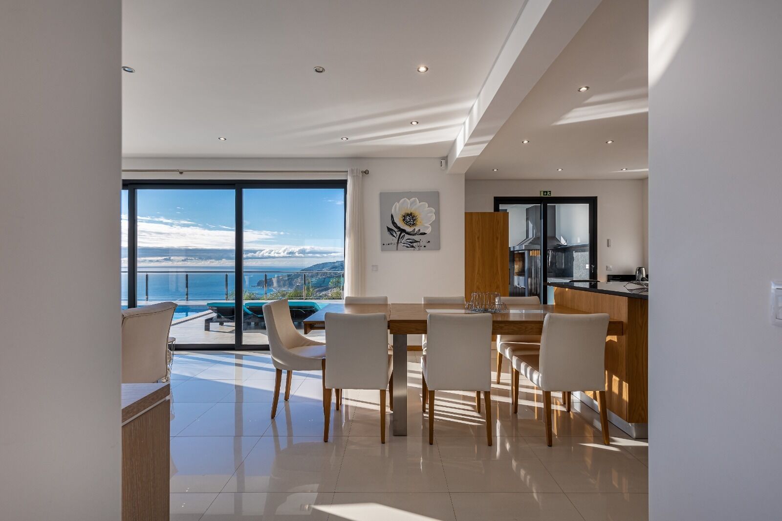 Un comedor moderno con vista al mar, una cocina con una isla grande y una mesa de comedor con sillas.