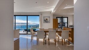 Un comedor moderno con vista al mar, una cocina con una isla grande y una mesa de comedor con sillas.