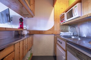 A compact kitchen with wooden cabinets, a microwave, a kettle, and a dishwasher.