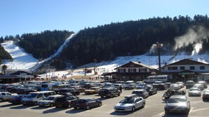 A parking lot with cars, a building with a sign reading "BRASSERIE LE GRAND HAUT", and a ski slope in the background. - STUDIO No. 15, on the station (Gérardmer)