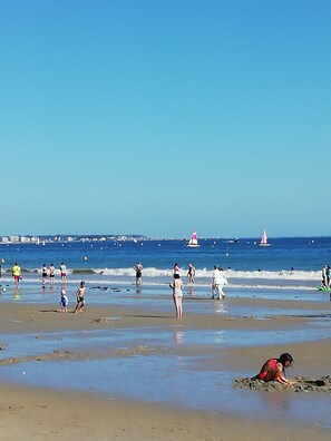 A beach with people walking and playing, boats in the water, and a lighthouse in the distance. - Entire apartment, full of charm, close to shops, beach and forest (La Baule)