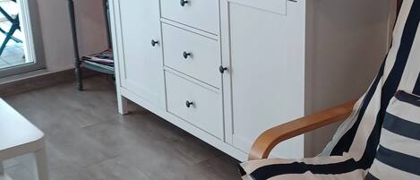 Quarto com um armário branco, televisão, luminária e cadeira listrada.