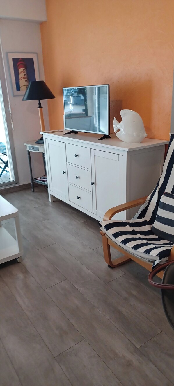 A room with a white cabinet, a television, a lamp, and a striped chair.