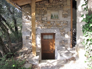 Un bâtiment en pierre avec une porte en bois et une petite étagère où sont posées des bouteilles.