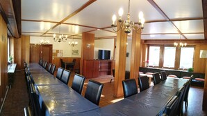 Une grande salle de conférence avec une longue table, de nombreuses chaises et un téléviseur à l’arrière-plan.