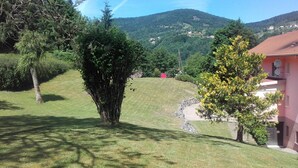 Une zone herbeuse avec un arbre, un bâtiment doté d’un toit rouge et une colline en arrière-plan.