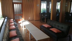 Une pièce avec un plancher en bois, un canapé en cuir noir agrémenté de coussins roses, une table blanche et un coin repas avec des chaises et une table.