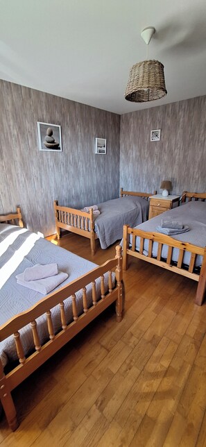 Una habitación con tres camas de madera, una lámpara colgante de tejido y dos cuadros en la pared.