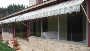 Una casa con fachada de piedra, ventanas amplias con cortinas y plantas en macetas en el patio.