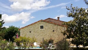 Un edificio de piedra con techo de tejas, una ventana pequeña y una campana en la pared.