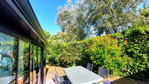 A patio area with a table and chairs, surrounded by lush greenery and trees. - OLD: charming house 100m from the beach (2 bedrooms, 2 bathrooms) (Noirmoutier-En-L'île)