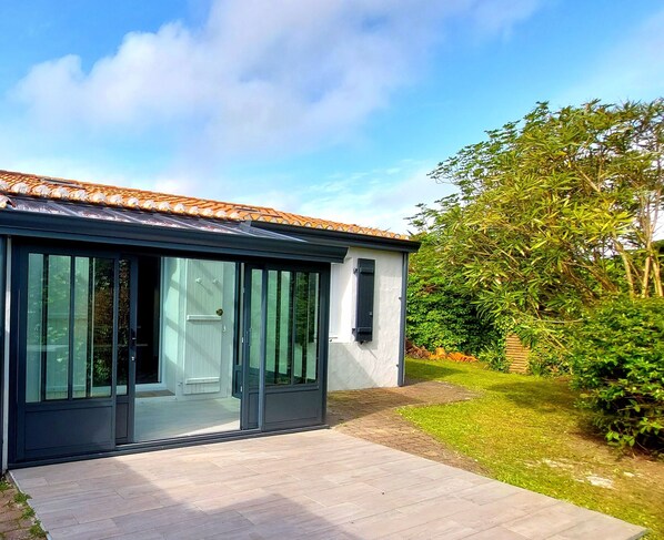 A modern house with a large sliding glass door entrance, a tiled roof, and a well-maintained garden.