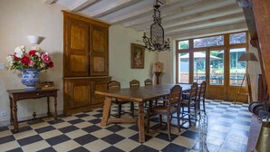 A dining area with a checkered floor, wooden table, chairs, a vase with flowers, a wooden cabinet, and a chandelier. - Family home in a wooded park with swimming pool near Futuroscope (Thurageau)