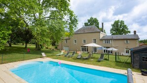 A swimming pool with lounge chairs and umbrellas, surrounded by a well-maintained lawn and a large house with a chimney. - Family home in a wooded park with swimming pool near Futuroscope (Thurageau)