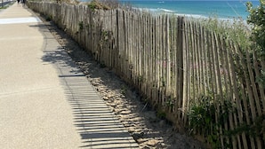 Eine Küstenstraße mit Holzzaun, blauem Himmel und dem Meer im Hintergrund.