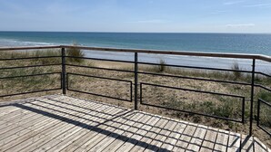 Eine Holzterrasse mit Metallgeländern, die auf einen Strand blickt.