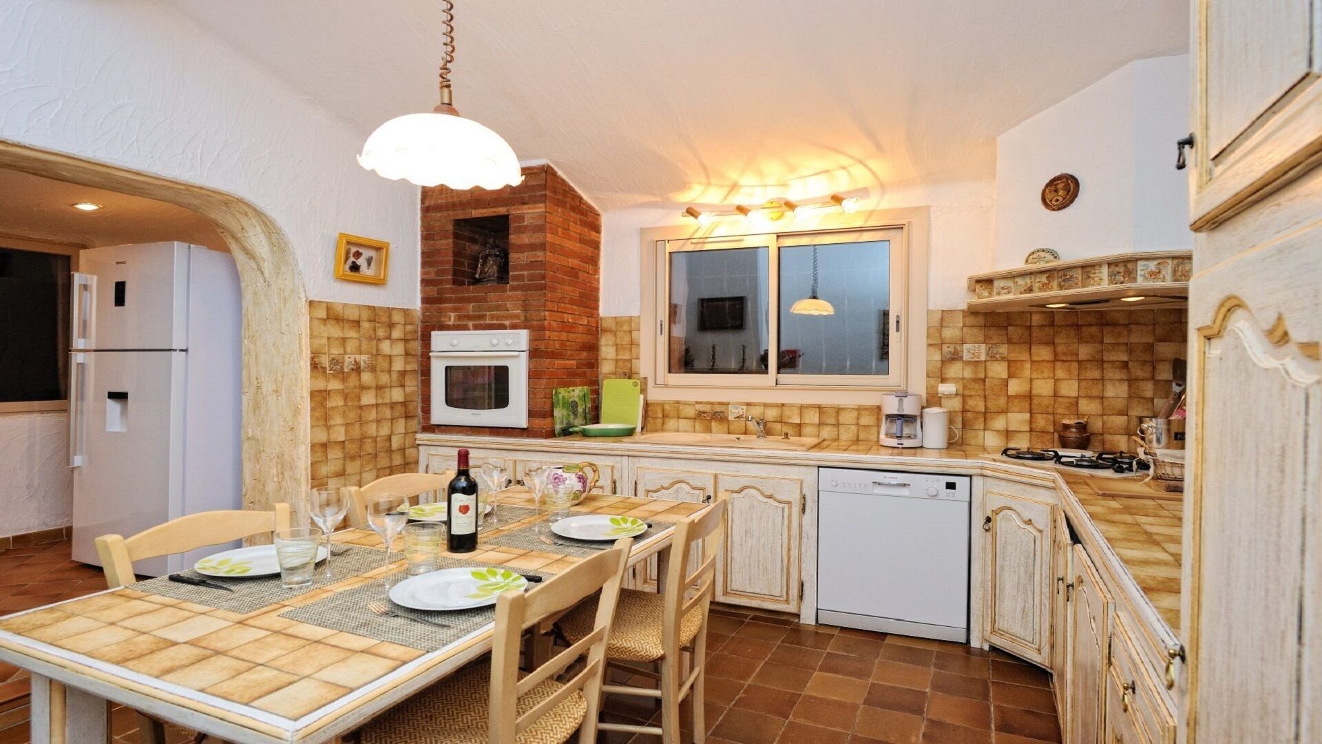 Eine kompakte Küche mit Esstisch, Stühlen, einem Kühlschrank, einem Backofen, einem Geschirrspüler und einem Fenster mit Aussicht.