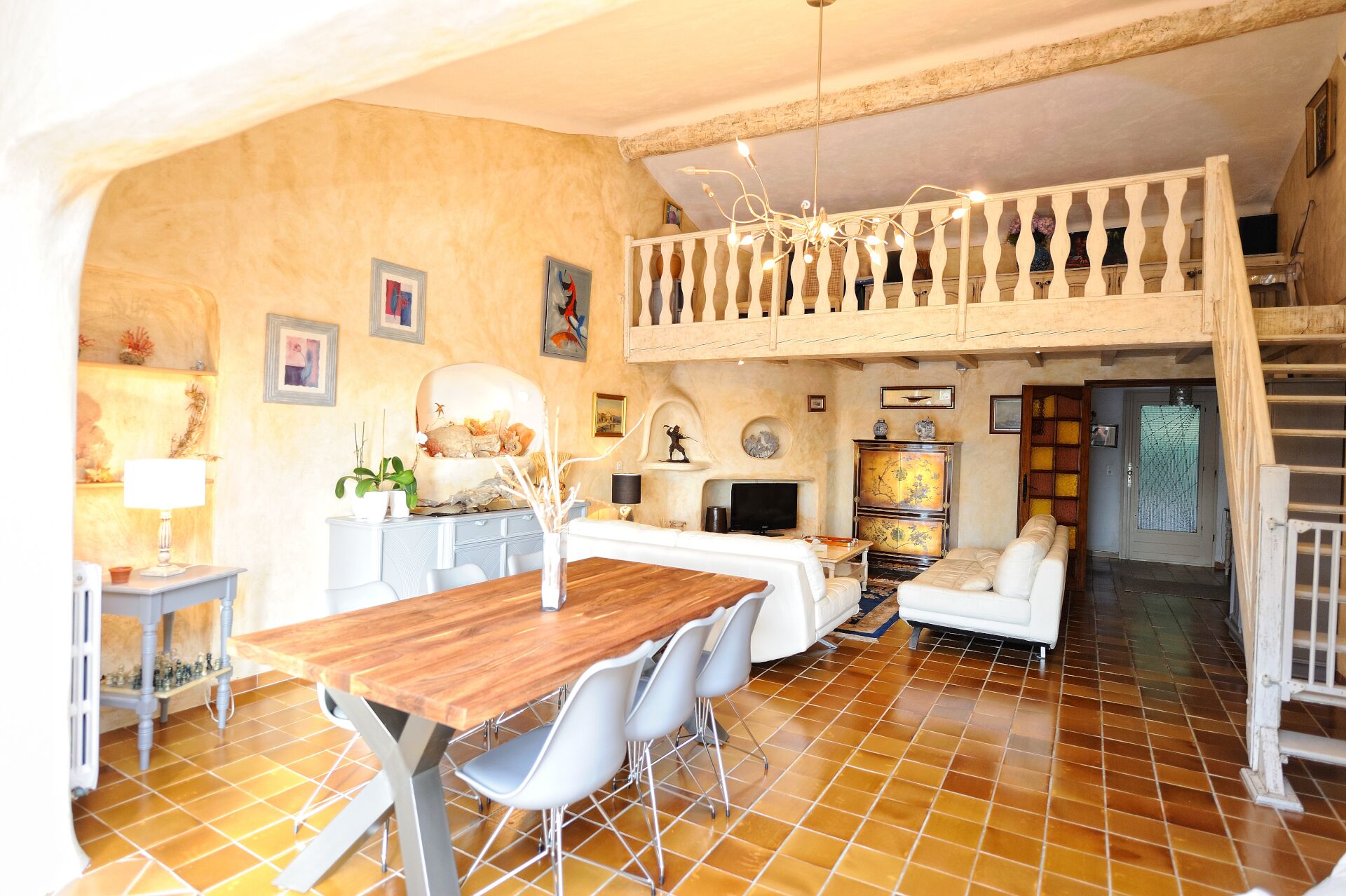 Un vaste espace de vie comprenant une table à manger en bois, des canapés blancs et un balcon doté d’une balustrade.