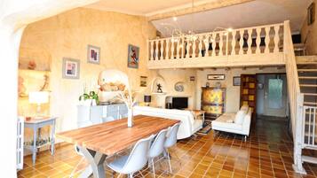 Un vaste espace de vie comprenant une table à manger en bois, des canapés blancs et un balcon doté d’une balustrade.