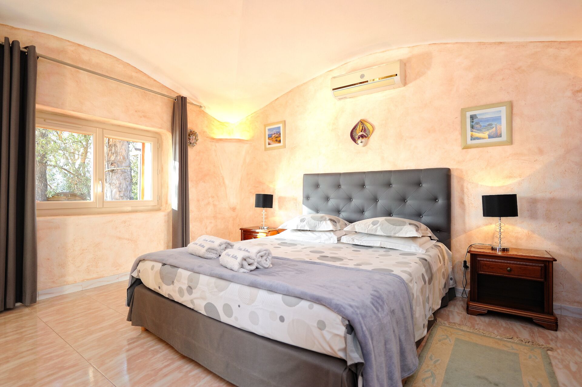 Un dormitorio con una cama grande, dos mesitas de noche, una ventana con cortinas y un equipo de aire acondicionado en la pared.