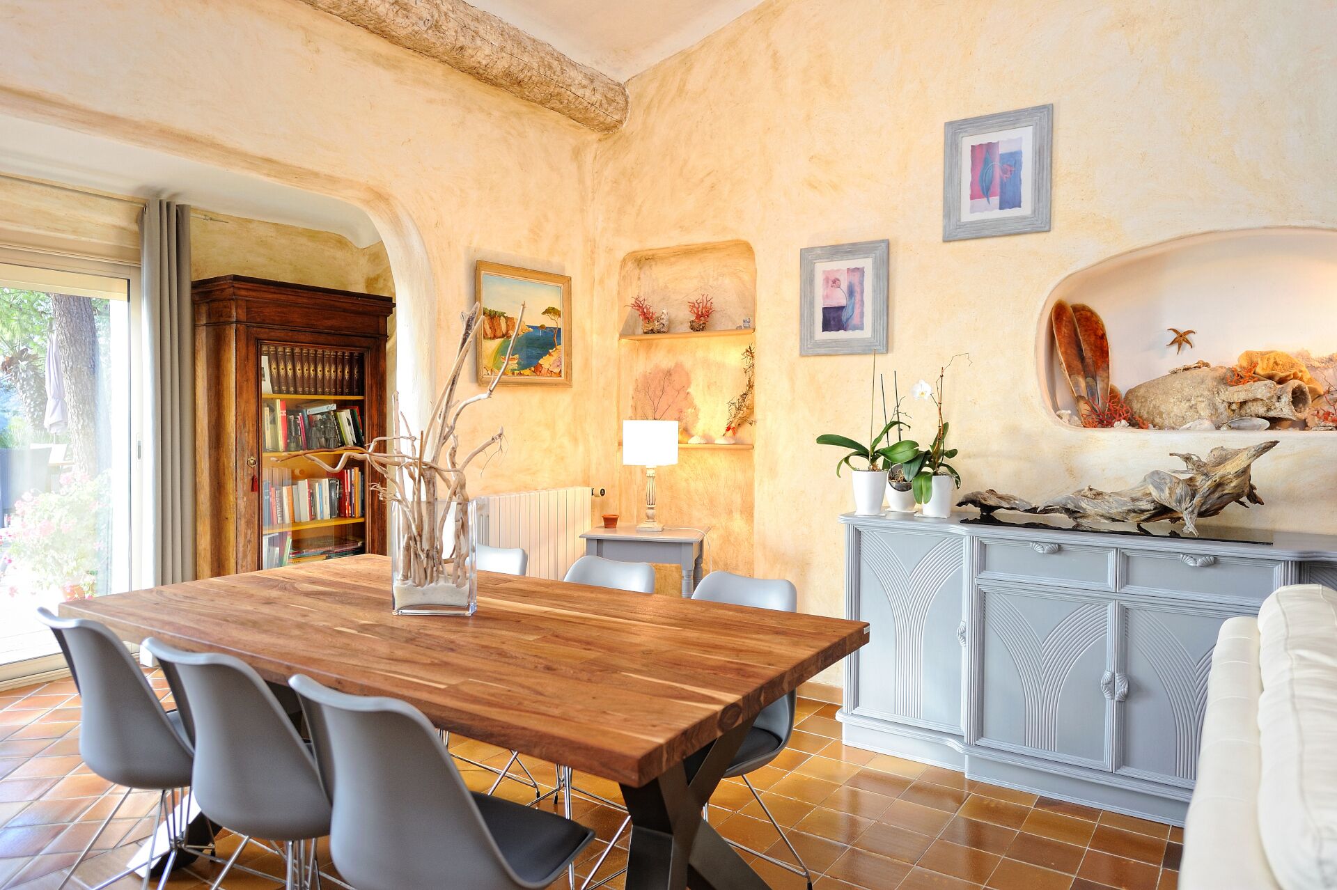 Un espace repas comprenant une table en bois, des chaises modernes, une bibliothèque, des œuvres d’art décoratives au mur et un meuble agrémenté d’éléments naturels.