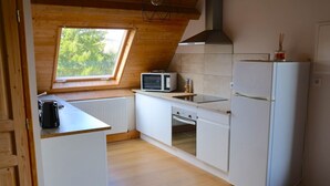 Une cuisine compacte avec des meubles blancs, un four à micro-ondes, une cuisinière et un réfrigérateur. Un puits de lumière apporte un éclairage naturel, et le sol est en bois.