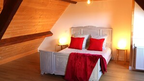 Une chambre avec un plafond en pente, un lit avec une literie rouge et blanche, deux lampes de chevet et un radiateur.