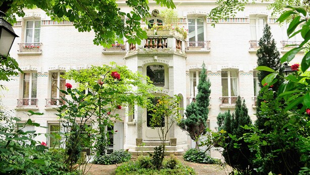 A white building with a central entrance, surrounded by a garden with various plants and a pathway leading to the entrance. - atypical design studio, 2 terraces (Paris)