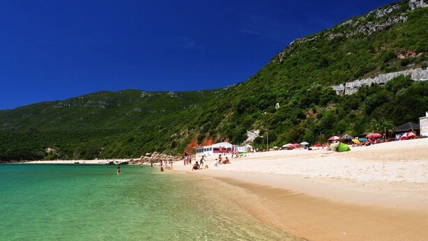 A beach with clear turquoise water, sandy shore, and lush green hills in the background. - holiday house with pool in azeitao (azeitao)