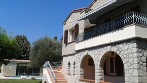 A stone building with a staircase leading to an upper level, arched doorways, and a balcony with metal railings. - Beautiful Provencal Stone Villa with Large Pool and Pool House (Grasse)
